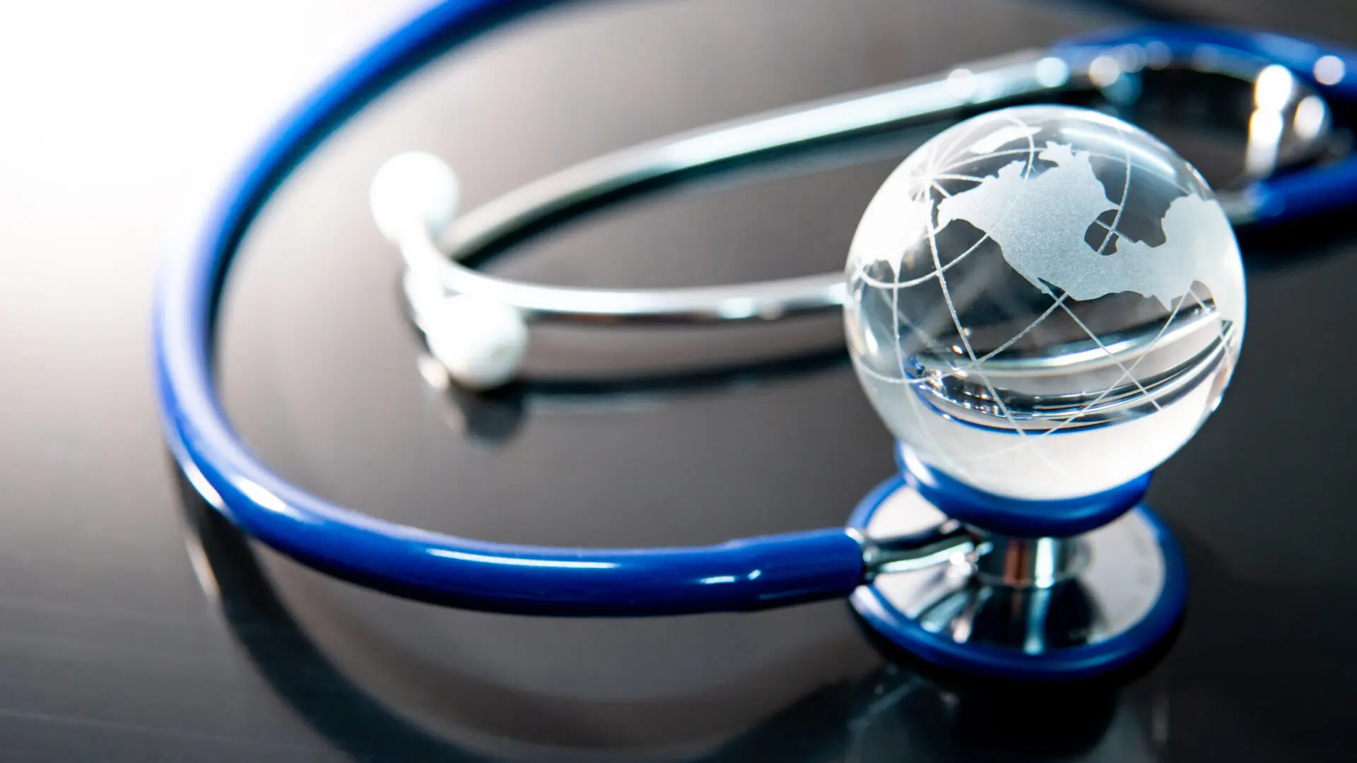 Global healthcare concept. World globe crystal glass on blue stethoscope on glossy desk. Health and medical science. Worldwide wellness business